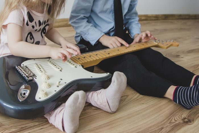 Zwei Kinder haben eine E-Gitarre auf dem Schoß und spielen gemeinsam